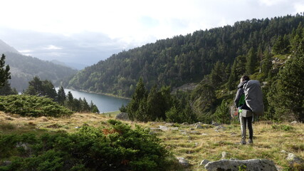 Hombre mirando a lago con montaña, bosque y nibes