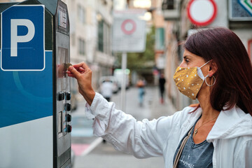 adult woman with mask insert coins in park meter