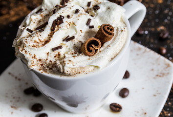 Cup of coffee with cinnamon sticks, whipped cream and chocolate sprinkles. Cozy winter hot beverage.