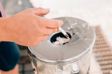 A guy with a cigarette in his hands throws it in the trash.