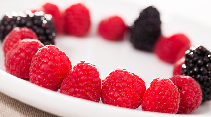 raspberries and blackberries laid out on a white plate in circle