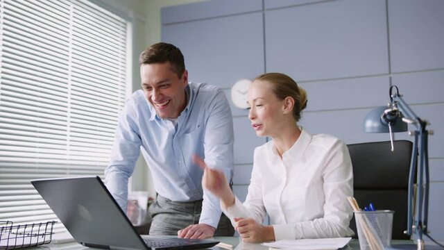 young man and woman work together in office with laptop on desk. make high five, successful teamwork. looks positive and cheerful, smiles. 