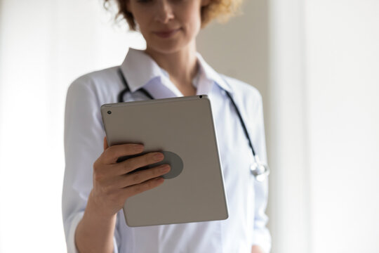 Close Up Focused Woman Professional Doctor Holding Digital Tablet, Looking At Screen, Serious Therapist Physician Gp Working Online, Analyzing Patient Medical Checkup Results, Telemedicine