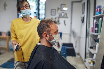 Hairdresser and customer in a salon with medical masks during virus pandemic. Working with safety mask.