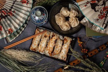 Material of traditional chinese fried dumplings(also called gyoza,pot sticker) on table with black background and decorate with chinese style fans and tea cup.