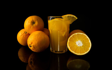 Glass of fresh orange juice surrounded with fruits on black background.