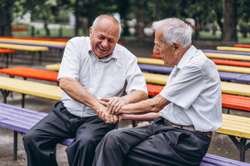 Two old senior adult men have a conversation outdoors in the city park. - Powered by Adobe