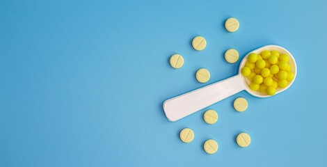 A dosed spoon filled with yellow vitamin C on the background of tablets. Free space for text