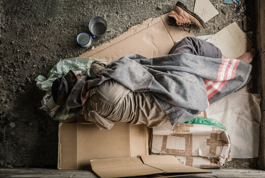 Old homeless man wearing sweater and blanket sleeping on cardboard seeking help because hungry and food beggar from people walking pass on street. Poor man homeless and depression concept.