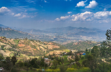 Fototapeta na wymiar The eastern part of the Kathmandu valley, on a sunny day, with the hills and foothills of the Himalayas, terraces with agricultural crops, against the backdrop of a blue sky and clouds.