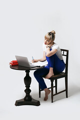 Focused young female student sitting at desk working or studying remotely online writing notes while looking on laptop screen. Distant learning or remote work from home. Isolated on white background.