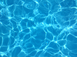 Fototapeta na wymiar Blue water of a swimming pool in summer with reflections of sunlight in rippling waves