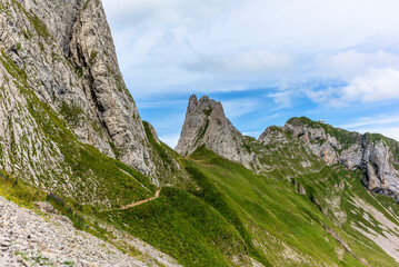 Hikers on the steep path leading to the majestic  Schaefler peak in the  Alpstein mountain range around the Aescher cliff in Appenzell, Switzerland