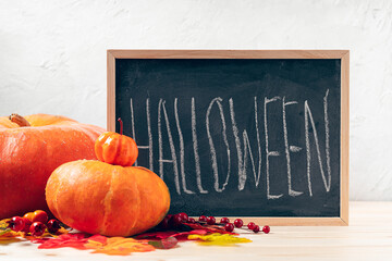 Pumpkins, berries and fallen leaves with chalk inscription halloween on blackboard frame on wooden background. Seasonal autumnal and Design background.