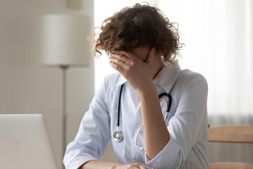 Close up unhappy stressed young woman doctor covering face with hand, upset worried therapist...