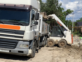 Heavy machinery at a construction site. Loader and truck during unloading. Unloading of building materials.