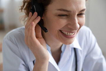 Close up smiling young woman doctor wearing headset with microphone working online, friendly...