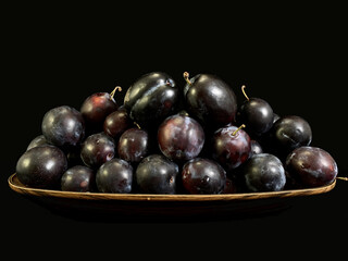 Blue plums on a black background. Heap of ripe plums in a plate. Fruit tree fruit.
