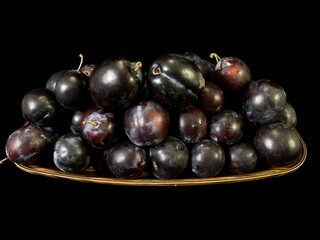 Blue plums on a black background. Heap of ripe plums in a plate. Fruit tree fruit.