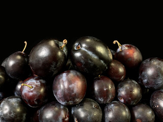 Blue plums on a black background. Heap of ripe plums in a plate. Fruit tree fruit.