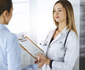 Young woman-doctor and her patient are discussing patient's current health examination, while...