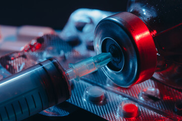 Syringe and pills in colored light.