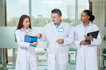 Mature experienced doctor helping intern to make diagnosis when thay walking in hospital hall