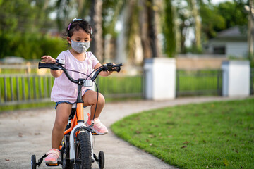 Obraz premium Cute little girl with protective face mask riding bicycle at village. 
