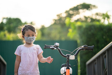 Cute little girl with healthy face mask standing beside her bicycle at village. 
