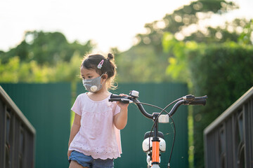 Cute little girl with healthy face mask standing beside her bicycle at village. 
