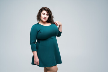 Plus size fashion model in green dress, fat woman on gray background, body positive concept