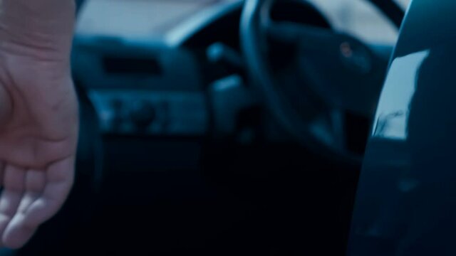 A man, a driver, a buyer opens the driver's seat door, gets behind the steering wheel of a new blue car and closes the door, then gets out of the car and closes the door. Closeup. Shallow depth of fie