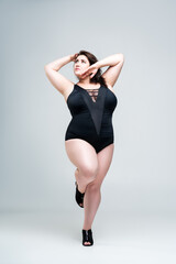 Sexy plus size fashion model in black one-piece swimsuit, fat woman in lingerie on gray background