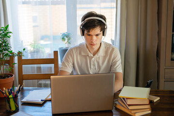 Young attractive guy is browsing at his laptop, sitting at home on the cozy beige sofa at home, wearing casual outfit