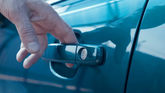A man, a driver, a buyer opens the driver's seat door by the key, gets behind the steering wheel of a new blue car and closes the door, then gets out of the car and closes the door by the key. Closeup