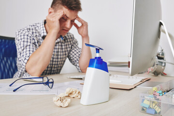 Hand sanitizer on desk of UI designer having headache after working all day long with difficult clients