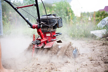 Man working in the garden with garden tiller. Garden tiller. Cultivating field at spring. Farmer...