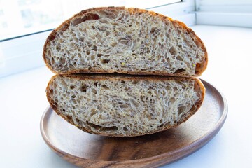Composition in bright sunlight. Two halves of round homemade yeast-free (whole grain) bread on a wooden plate. On a light background