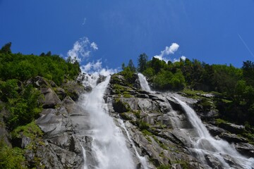 Fototapeta premium tall waterfall and green trees with blue sky in trentino
