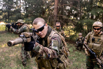 Focused armed soldiers in uniform carrying rifles and examining forest terrain