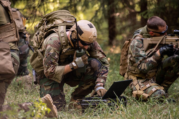 Busy soldier with backpack using military laptop while passing information through radio device in...
