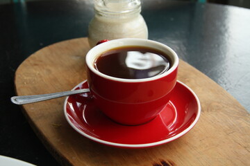 cup of strong coffee on a red plate with a spoon
