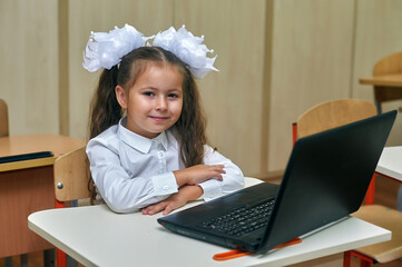 Portrait of an elementary school student in class with a laptop . Lesson in primary school, children at a safe distance