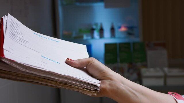 Nurse holding out card with results of examination. Stock footage. Close-up of nurse giving results of examination and tests on dark background of hospital. Results of medical examination