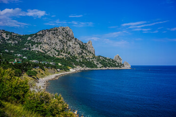 Rock covered with green vegetation hanging over the calm blue sea