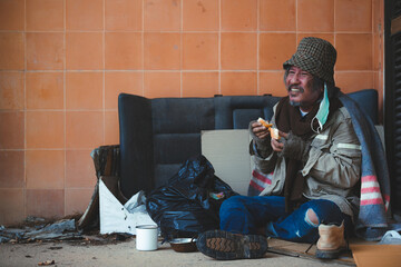 Old homeless man in a green cloak holds bread, hands where people give bread or share food to help...