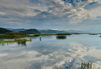 lake with sky reflection and reeds surrounded by mountains