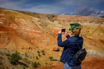 Female tourist takes pictures of amazing natural phenomenon on her smartphone. Colorful mountains in the Altai. Travel in Russia. Unknown planet.