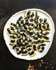farfalle pasta cuttlefish ink black, durum wheat semola on a plate macaroni from semola durum wheat on the table serving portion size top view place copy space
