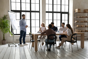 Full length skilled young speaker standing near whiteboard with statistics sales data, presenting...
